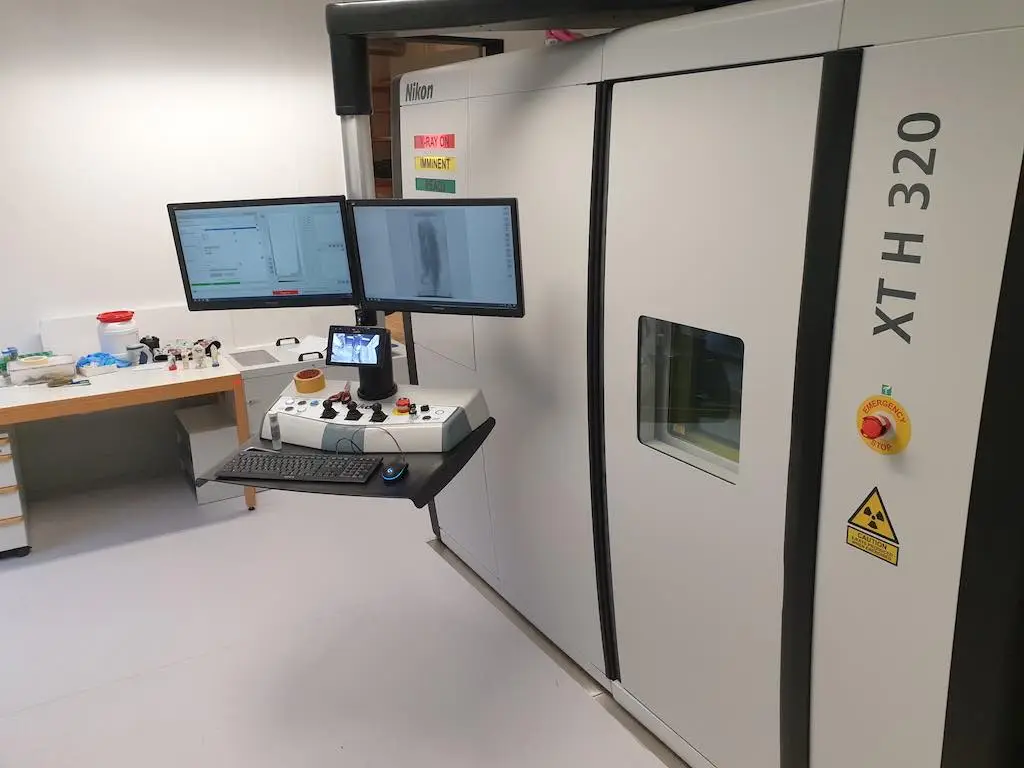 A room-sized micro CT scanner with an associated work station, keyboard, controls, and dual monitors