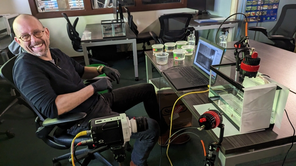 Person, die an einem Schreibtisch vor einem Computer und neben einer Filmausrüstung sitzt