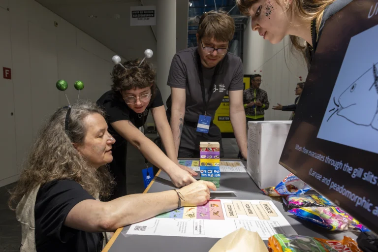 Photo of a woman kneeling at a table to play a game with an adult nearby pointing out something on the table